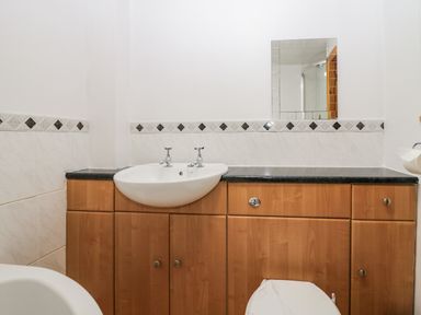 A bathroom with a sink, wooden cabinets, a mirror, and part of a toilet at Time and Tide in Arnside