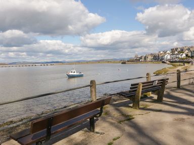 Two benches by the waterfront with a boat on the water and buildings in the distance at Time and Tide in Arnside