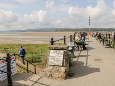A pier with benches and people sitting near a sandy beach and water at Arnside Pier in Arnside