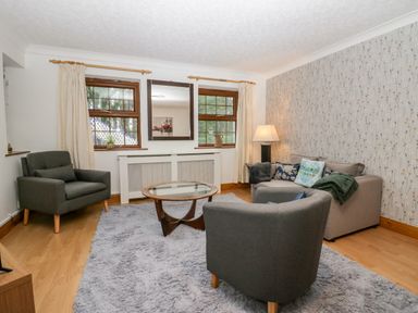 A living room with two grey armchairs a grey sofa a glass coffee table and a lamp at Time and Tide in Arnside