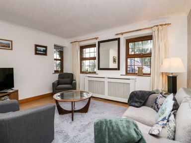 A living room with gray chairs a glass coffee table and a sofa with pillows and blankets at Time and Tide in Arnside