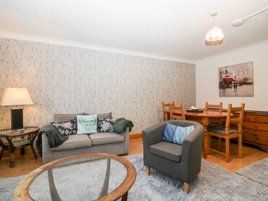 A living room with a grey sofa and armchair a wooden dining table and chairs and a glass coffee table at Time and Tide in Arnside