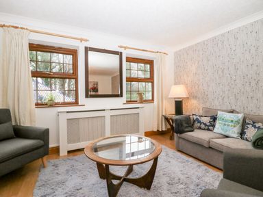 A living room with two windows a mirror a round glass coffee table sofas and a lamp at Time and Tide in Arnside