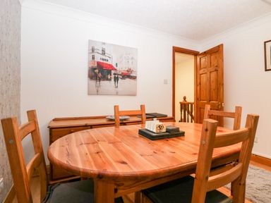 A dining room with a wooden table and chairs a sideboard and a painting on the wall at Time and Tide in Arnside