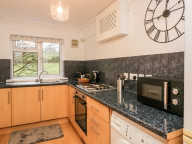 A kitchen with wooden cabinets a black countertop a window and appliances at Time and Tide in Arnside