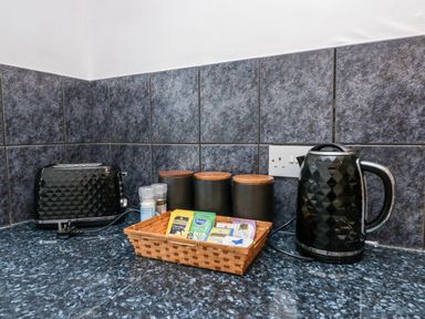 A kitchen countertop with a toaster, electric kettle, spice containers, and a basket of tea bags at Time and Tide in Arnside