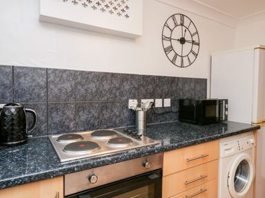 A kitchen counter with a stove kettle microwave washing machine and utensils at Time and Tide in Arnside