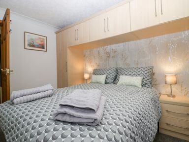 A bedroom with a double bed towels on the bed built-in overhead cabinets and bedside tables with lamps at Time and Tide in Arnside