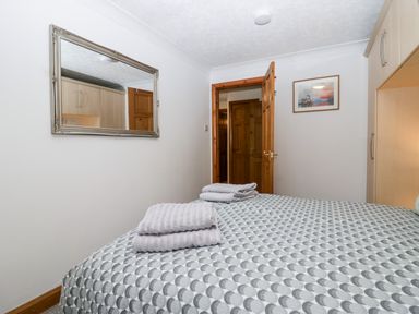 A bedroom with a bed covered in patterned bedding towels on the bed a mirror on the wall an open wooden door and a framed picture on the wall at Time and Tide in Arnside