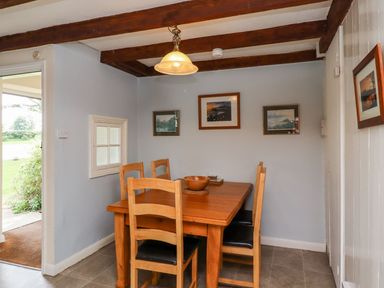 A dining room with a wooden table and four chairs under exposed beams at Cherry Tree Cottage in Fallodon near Embleton
