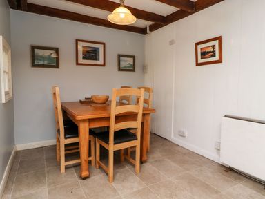 A dining area with a wooden table and four chairs and framed pictures on walls at Cherry Tree Cottage in Fallodon near Embleton
