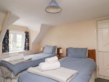 A bedroom with two single beds blue checked bedding and folded towels on beds at Cherry Tree Cottage Fallodon near Embleton