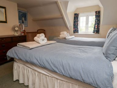 A bedroom with two single beds with checked bedding a dresser and a window with patterned curtains at Cherry Tree Cottage in Fallodon near Embleton
