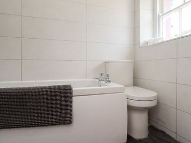 A bathroom with a bathtub a toilet and a window at Cherry Tree Cottage in Fallodon near Embleton