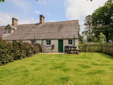 A small cottage with a green door and two windows with a grassy yard and outdoor table and chairs at Cherry Tree Cottage in Fallodon near Embleton