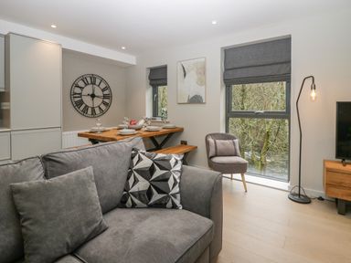 A living room with a gray sofa and patterned pillow next to a dining table set with plates and glasses at Brimstone Backbarrow near Ulverston