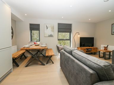 A dining area with wooden table and benches and a living room with grey sofa and TV at Brimstone Backbarrow near Ulverston