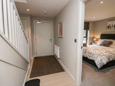 A hallway with staircase and a door next to a bedroom with a bed and nightstand lamp at Brimstone in Backbarrow near Ulverston