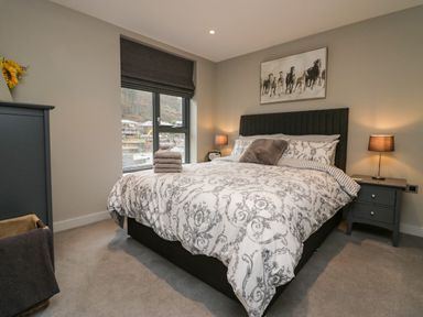 A bedroom with a patterned bedspread on a bed bedside tables with lamps and a window at Brimstone Backbarrow near Ulverston