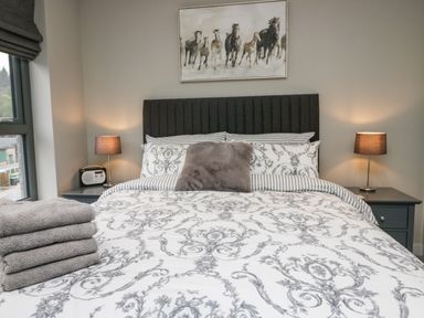 A bedroom with a bed with patterned bedding two bedside tables with lamps and a painting of running horses at Brimstone Backbarrow near Ulverston