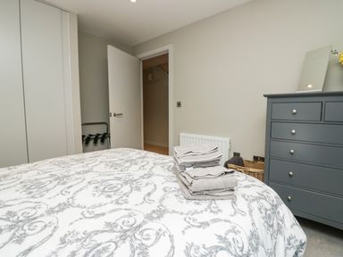 A bedroom with a bed with patterned duvet a stack of towels on it a gray chest of drawers and an open door at Brimstone in Backbarrow near Ulverston