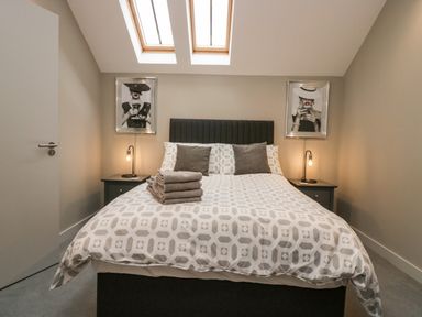 A bedroom with a bed with patterned bedding towels on bed two bedside tables with lamps two framed pictures on the wall at Brimstone Backbarrow near Ulverston