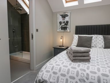 A bedroom with a bed and folded towels next to an open door leading to a shower at Brimstone in Backbarrow near Ulverston