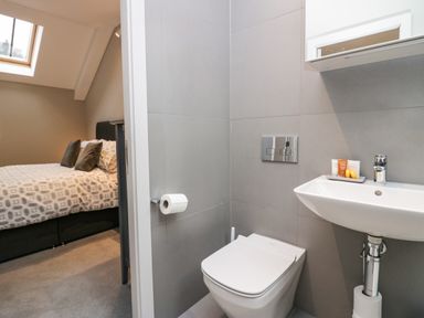 A bathroom with a toilet and sink next to a bedroom with a bed and pillows at Brimstone in Backbarrow near Ulverston