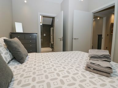 A bedroom with a bed featuring patterned bedding and towels stacked on top a dresser and two open doors one leading to a bathroom at Brimstone in Backbarrow near Ulverston