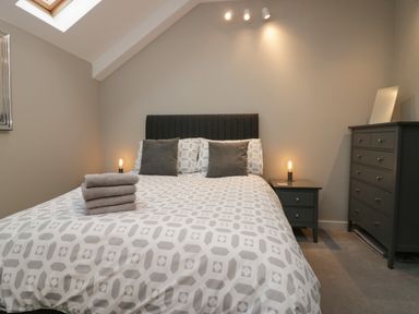 A bedroom with a bed with patterned duvet and folded towels a nightstand with a lamp and a dresser with a mirror at Brimstone in Backbarrow near Ulverston