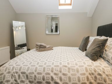 A bedroom with a bed with patterned bedding two pillows towels a standing mirror and a mirror on the wall at Brimstone Backbarrow near Ulverston