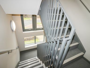 An indoor staircase with grey metal railings and two windows showing an outside view at Brimstone in Backbarrow near Ulverston