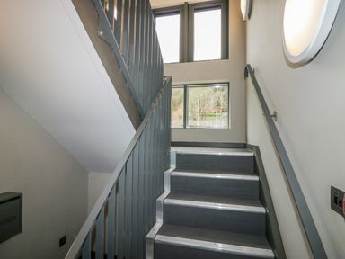 A stairwell with metal railings and windows showing trees outside at Brimstone Backbarrow near Ulverston