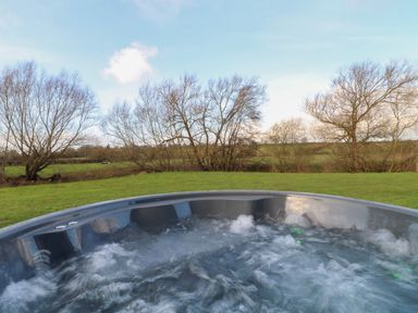 A bubbling outdoor hot tub with grass and leafless trees in the background at Squirrel's Nest in South Luffenham near Edith Weston