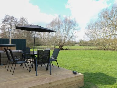 An outdoor deck with a table and chairs under a large umbrella next to a grassy field at Squirrel's Nest in South Luffenham near Edith Weston