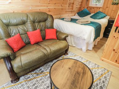 A room with a green leather sofa with three red cushions a bed with teal pillows and towels and a round wooden coffee table at The Poddy in Bushton near Lyneham