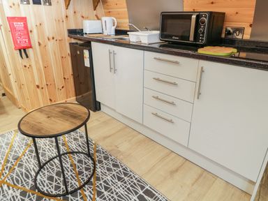 A kitchen area with white cabinets a black countertop a microwave a kettle a toaster and a small round table on a patterned rug at The Poddy in Bushton near Lyneham