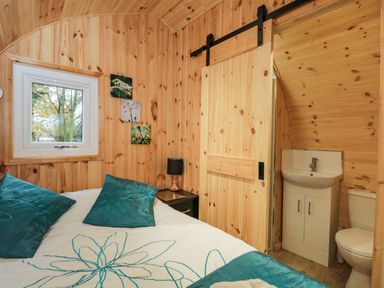 A bedroom with wooden walls a bed with teal pillows and a sliding door leading to a bathroom at The Poddy in Bushton near Lyneham