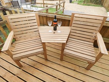 A wooden bench with an attached table holding a wine bottle and two glasses on a wooden deck at The Poddy in Bushton near Lyneham
