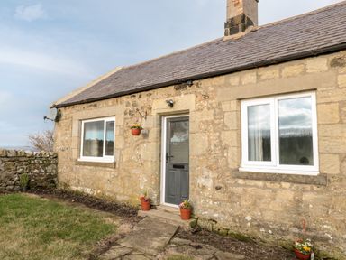 Stone house exterior with a door two windows flower pots on ground and hanging at Moorlaws Farm in Alnwick