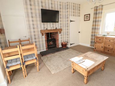 A living room with a wood burning stove under a wall mounted television and wooden furniture at Moorlaws Farm in Alnwick