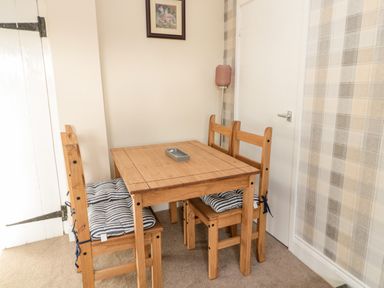 A wooden dining table with four chairs and striped cushions in a room with beige walls and plaid wallpaper at Moorlaws Farm in Alnwick