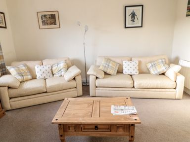 Two beige sofas with cushions and a wooden coffee table with a newspaper in a living room at Moorlaws Farm in Alnwick