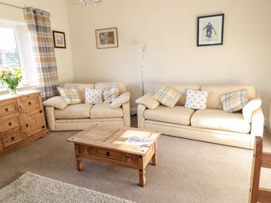 A living room with two beige sofas and a wooden coffee table with a newspaper at Moorlaws Farm in Alnwick