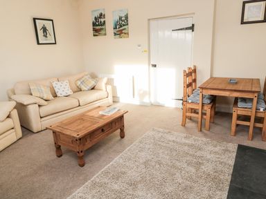 A living room with a beige sofa wooden coffee table small wooden dining table and chairs at Moorlaws Farm in Alnwick