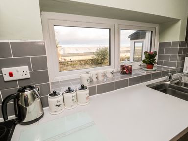 A kitchen countertop with a kettle three labeled jars cups a jar of dried flowers a small potted plant and a window overlooking an outdoor area at Moorlaws Farm Alnwick