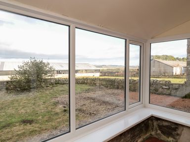 A corner window view of a grassy yard with stone walls and farm buildings at Moorlaws Farm in Alnwick