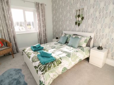 A bedroom with a double bed featuring leaf patterned bedding and towels on top at Moorlaws Farm in Alnwick