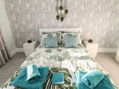 A bedroom with a bed with leaf patterned bedding two bedside tables with lamps and folded teal towels at Moorlaws Farm in Alnwick