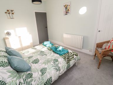 A bedroom with a bed with leaf patterned bedding and teal towels a chest of drawers and a wicker chair at Moorlaws Farm in Alnwick